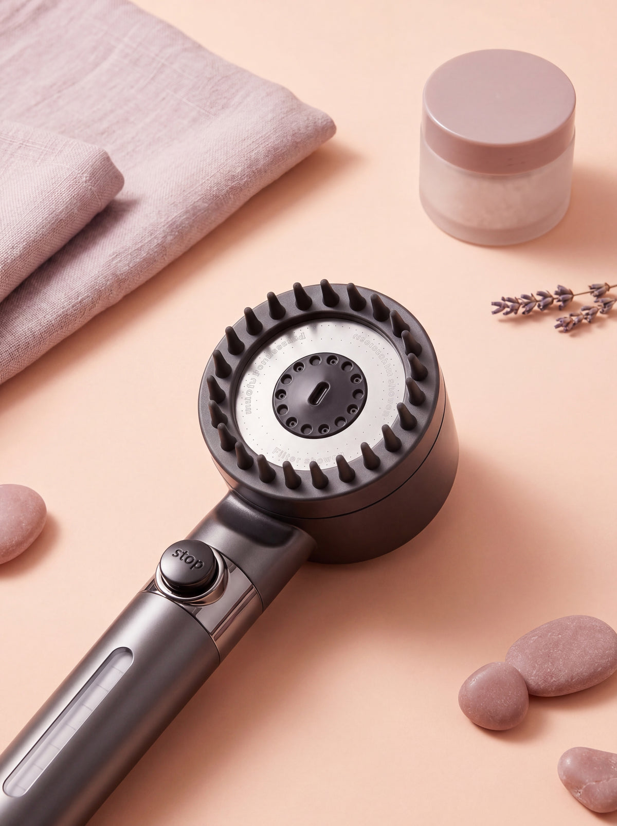 Close-up flat-lay of a silver filtered shower head scalp massager with micro-nozzles, on a soft peach surface.